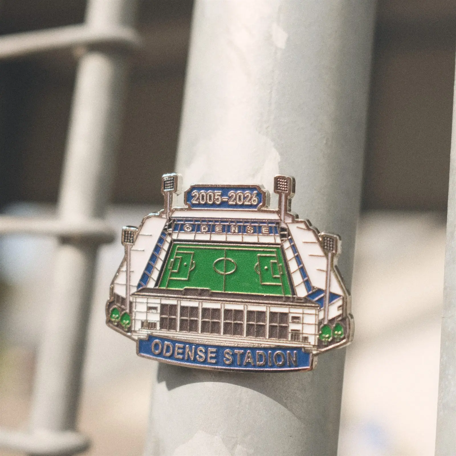 Emaljepin med Odense Stadion og årstallene 2005–2026 på en metalstang